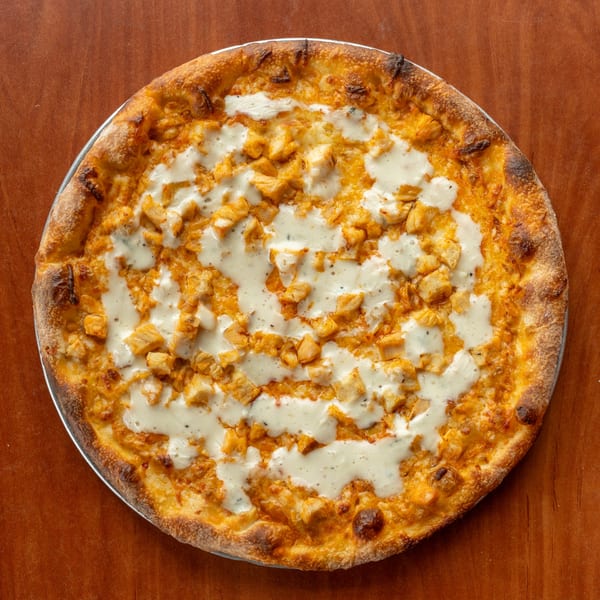 NY Pizza Patrol's Buffalo chicken pizza, topped with chicken pieces and white sauce, on a wooden table.