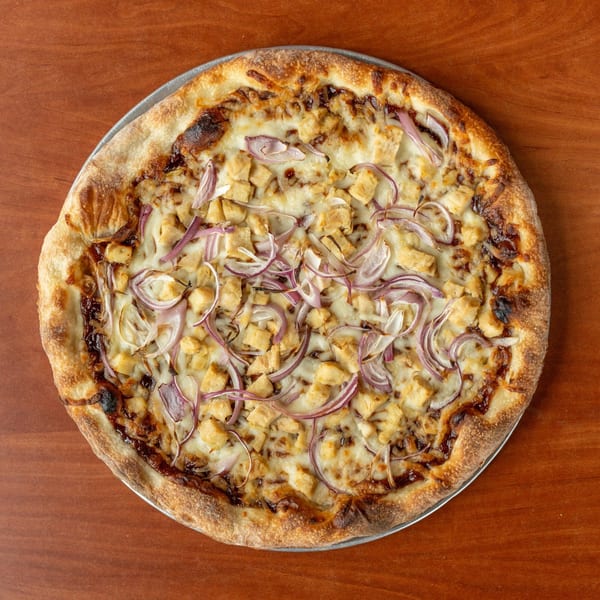 BBQ chicken pizza with red onions and mozzarella cheese on a wooden table.