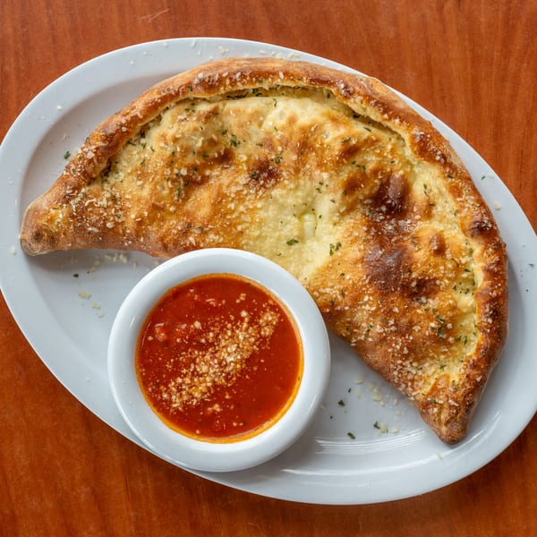 Golden-brown calzone sprinkled with herbs and cheese, served with a side of marinara sauce.
