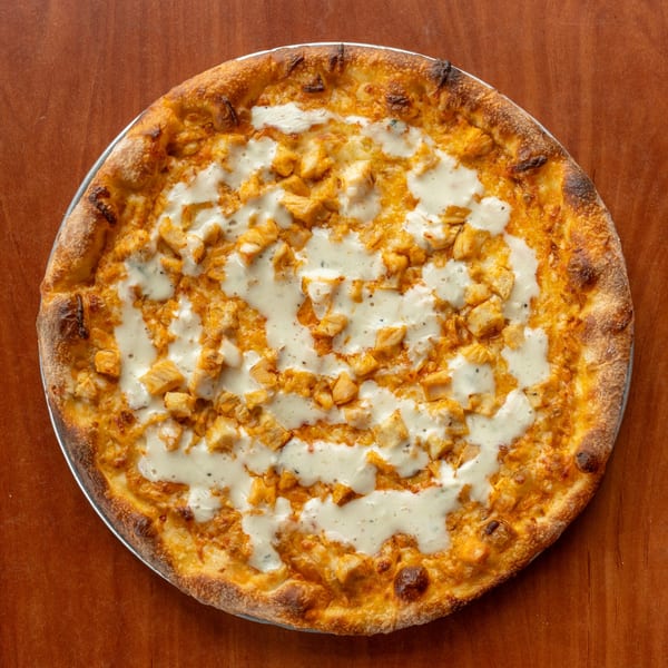 Overhead view of a buffalo chicken pizza with white sauce on a wooden table.
